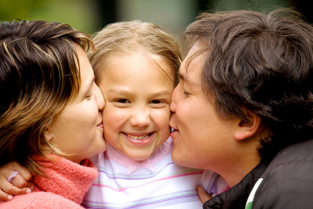 parents kissing daughter portrait looking very happy outdoors parents kissing daughter portrait looking very happy outdoors